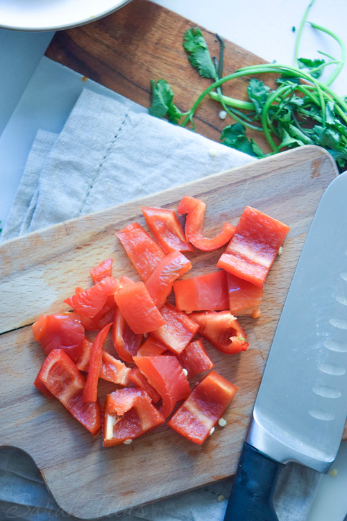 Chopped red pepper and cutting knife on cutting board with spinach on the side