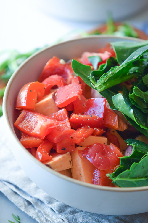 Large white bowl full of Sweet Potato Bake ingredients: sweet potato, red peppers and spinach all chopped up