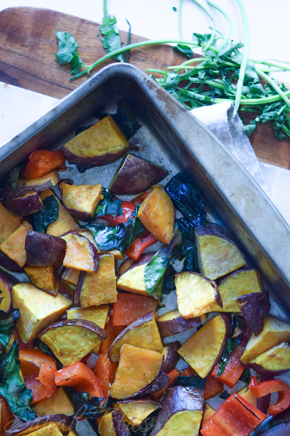 Sweet potatoes, red pepper and spinach pieces spread on a metal baking sheet ready to go in the oven