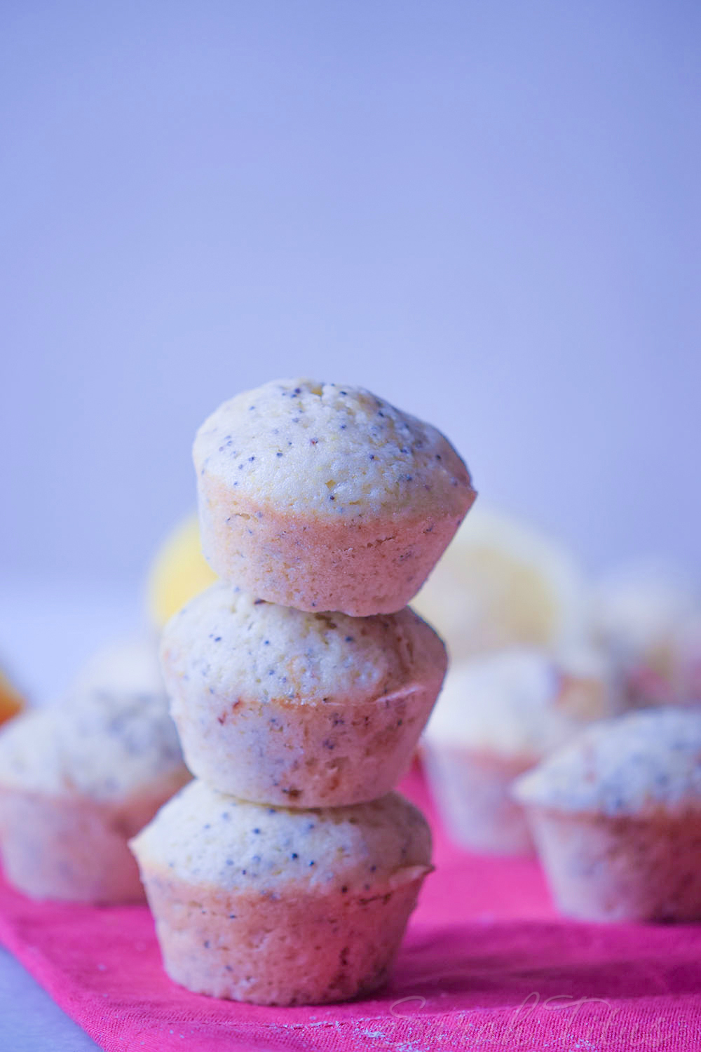Freshly baked lemon poppy muffins in a stack on a pink cloth napkin