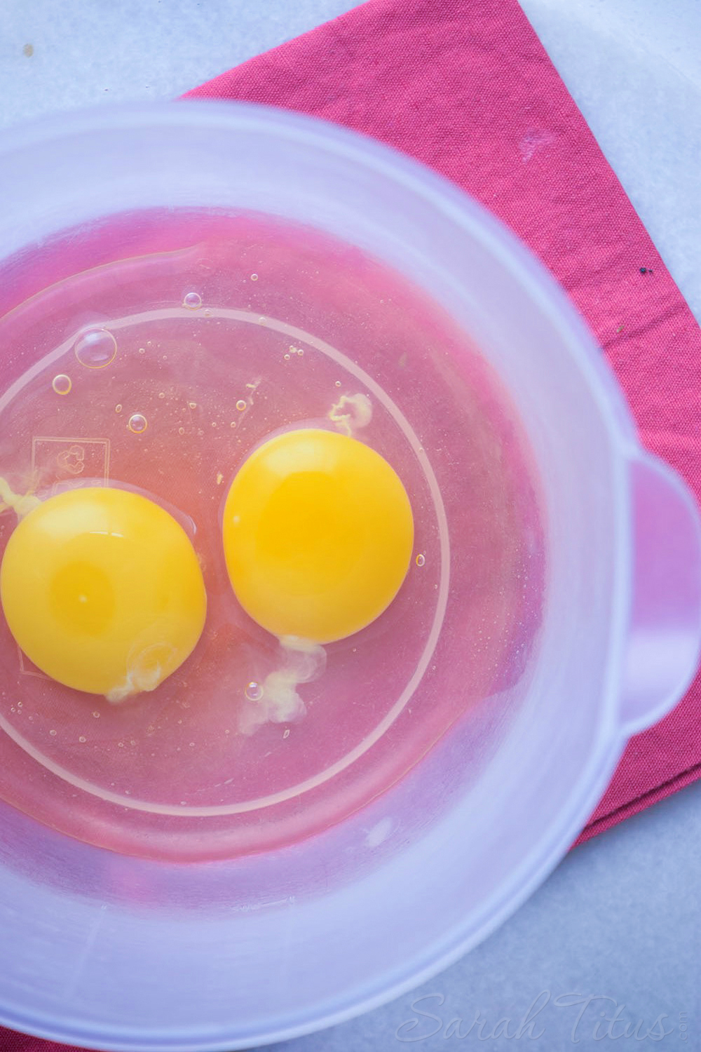 Eggs in a plastic bowl on a pink cloth napkin in preparation for making lemon poppy muffins