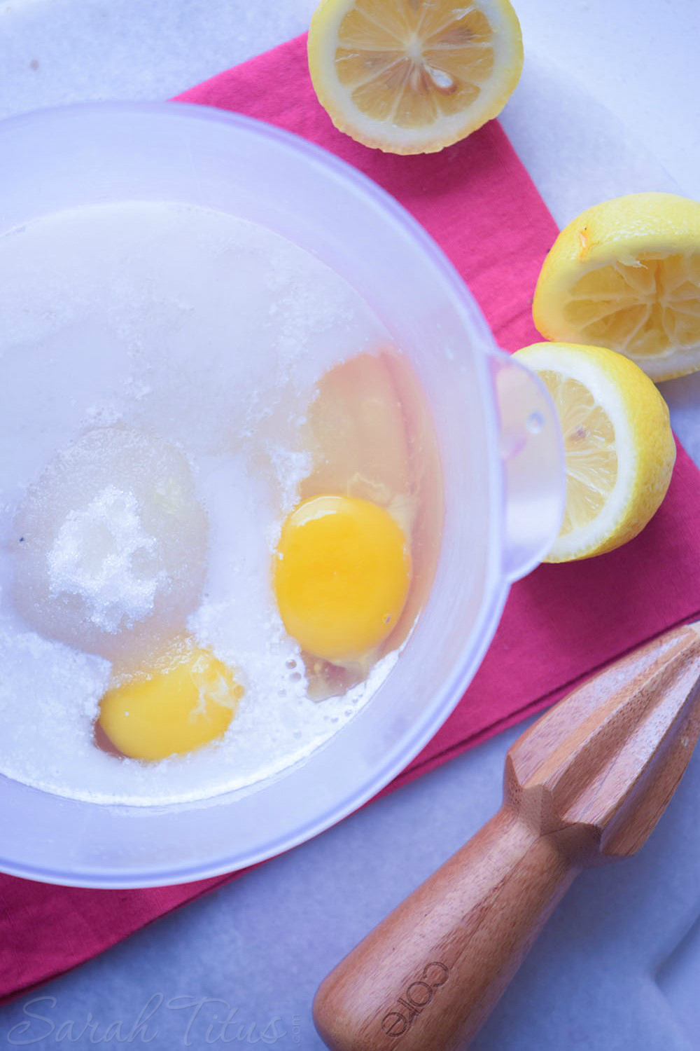 Plastic bowl with cracked eggs, sugar, milk, and lemon juice with fresh cut lemons on the side