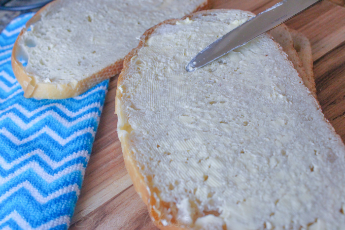 Spreading butter on sourdough bread on a wooden cutting board with blue striped cloth