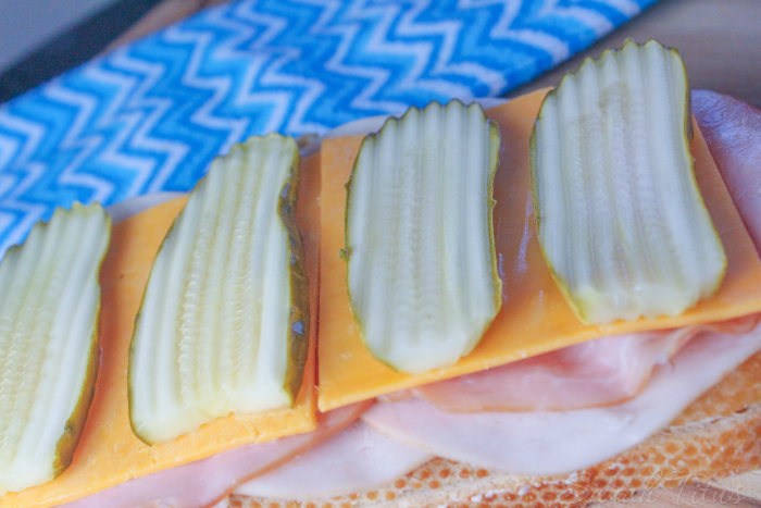 Adding cheese slices and pickle slices to sandwich on sourdough bread