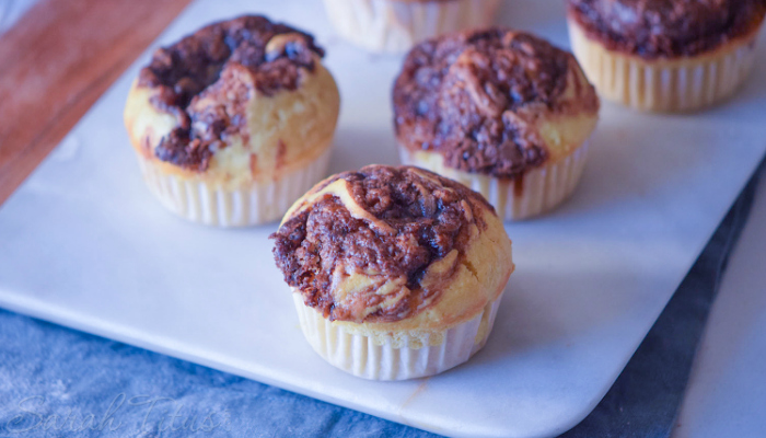 Freshly baked Nutella Swirl Muffins on a white cutting board on a blue cloth and wood table