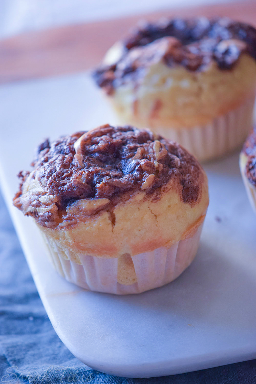 Freshly baked Nutella Swirl Muffins on a white cutting board on a blue cloth and wood table