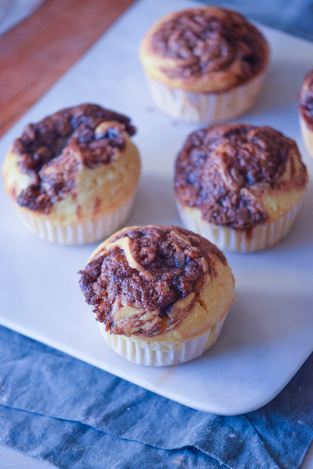 Freshly baked Nutella Swirl Muffins on a white cutting board on a blue cloth and wood table