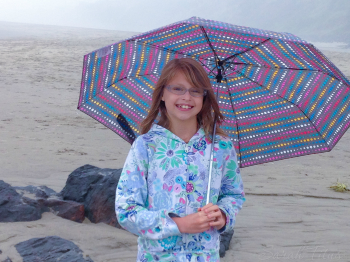 Girl with colorful umbrella on a cloudy beach on a road trip