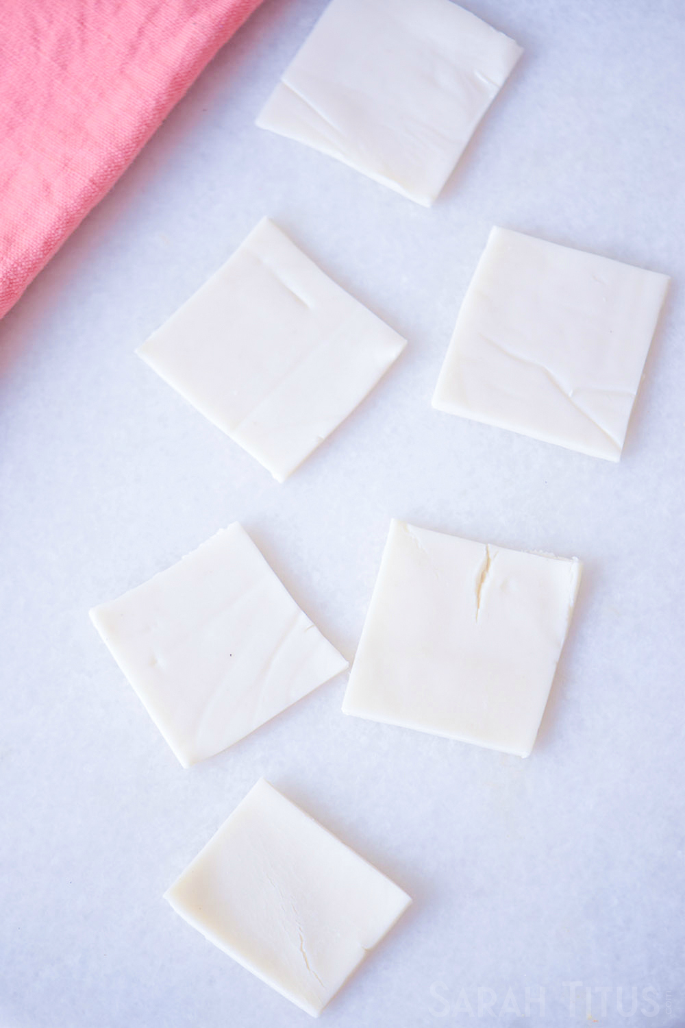 Puffed pastry sheets cut into little squares on a white counter with a pink towel