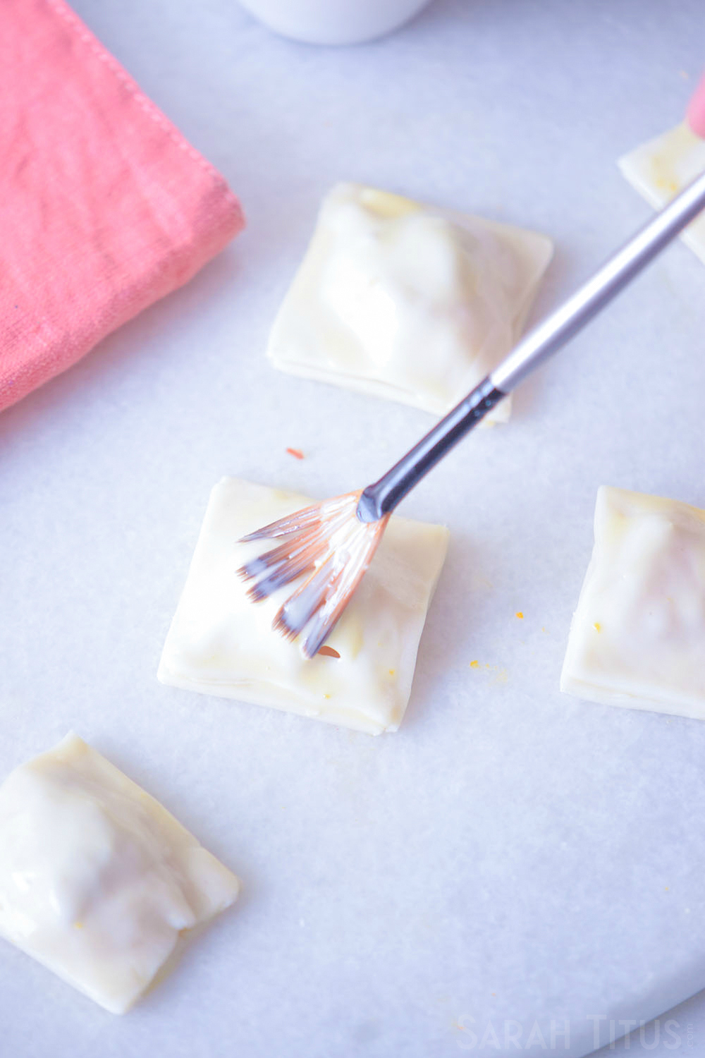 Pinched off puff pastry squared being brushed with an egg wash