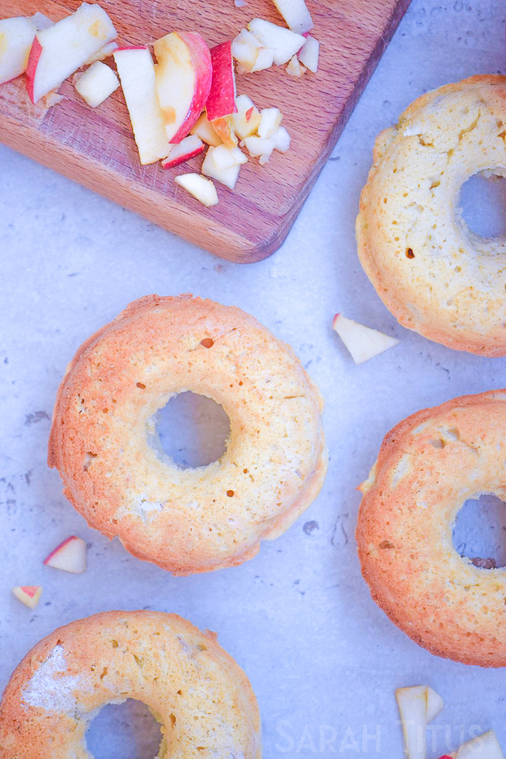 Beautifully browned finished baked apple doughnuts on the counter with a cutting board and chopped apples