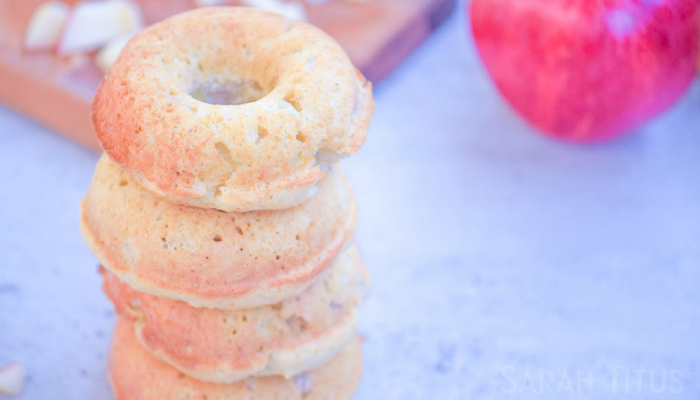 Baked apple doughnuts in a tall stack with a fresh apple and cutting board on the sides