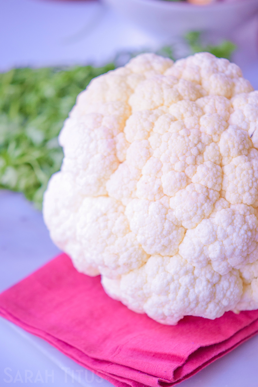 Beautiful white head of cauliflower on a pink towel with greenery in the background