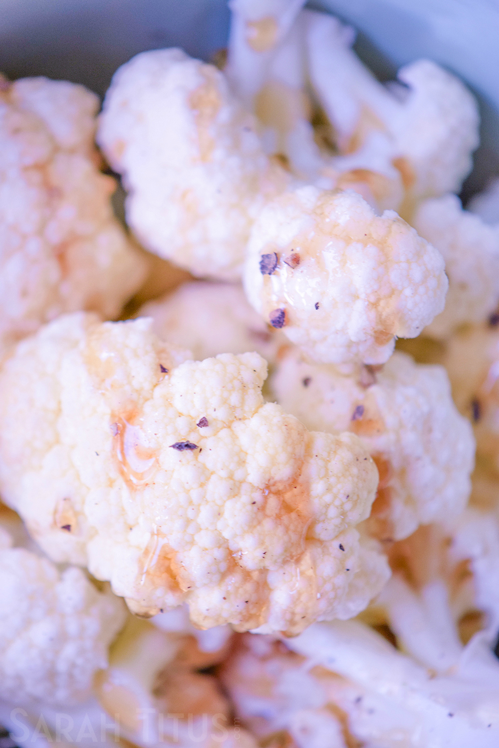 Topping the chopped cauliflower pieces with honey, olive oil, salt, pepper and garlic powder in a bowl