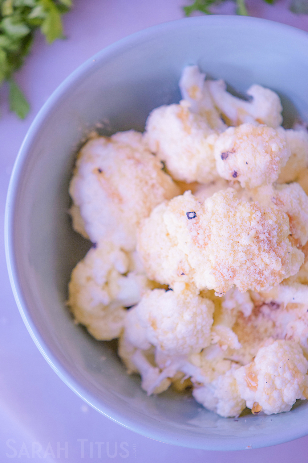 Topping the chopped cauliflower pieces with Parmesan cheese in a bowl