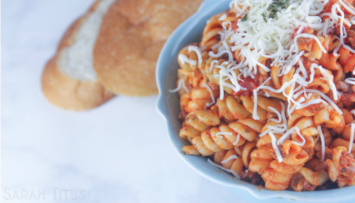 Spicy pasta with Parmesan cheese in a blue bowl with crusty bread