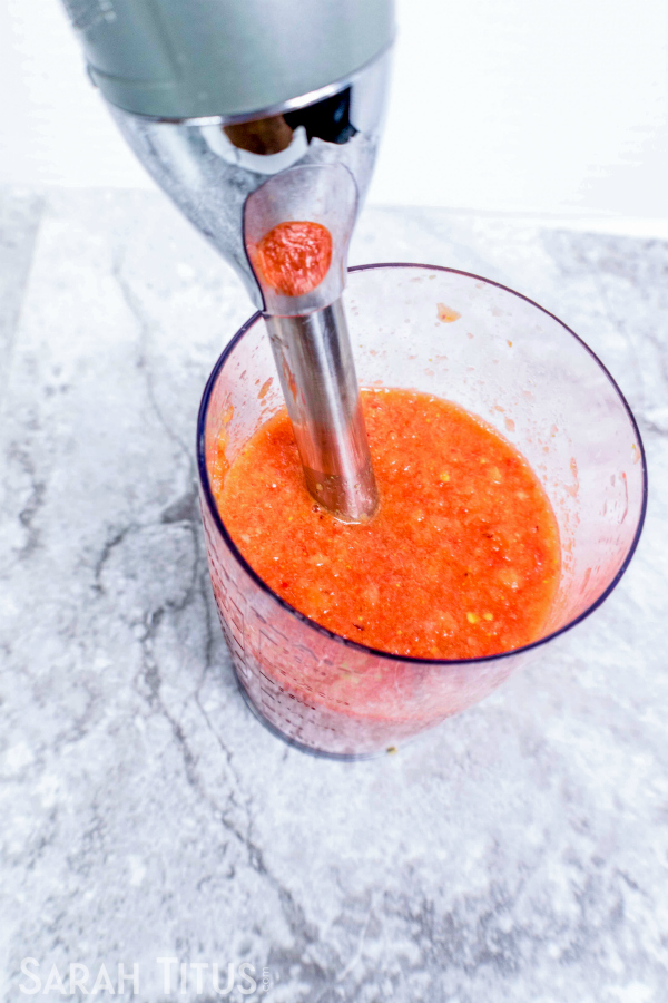 Blending together tomato, red bell pepper, onion, 1 of the garlic cloves and chicken base with a hand blender