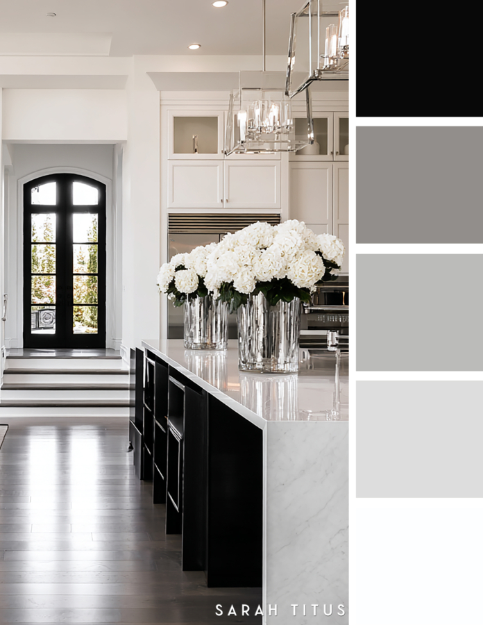 Bright black and white kitchen hallway with a marble island, black cabinetry, crystal lantern lights, white hydrangeas, and arched black doors in a gray and silver palette.