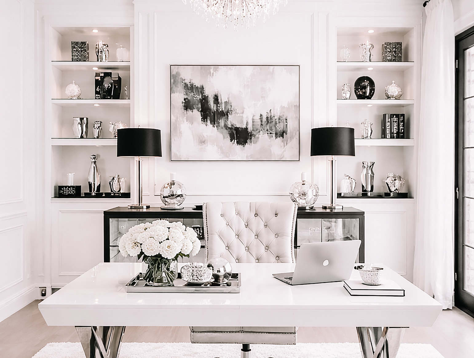 Black, white, and silver luxury home office with a white desk, tufted chair, black lamps, built in shelves, and elegant modern decor