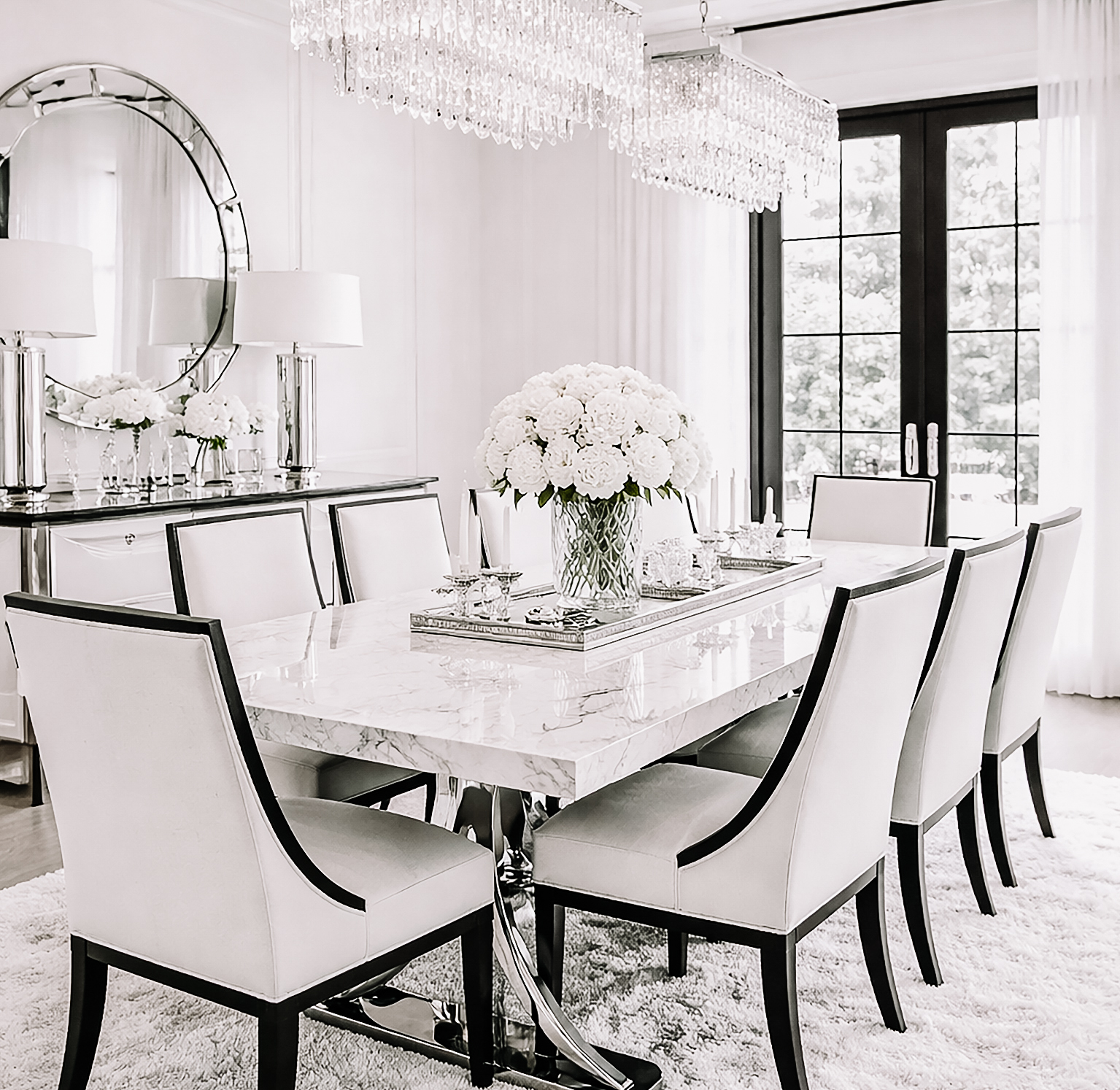 Black, white, and silver luxury dining room with a marble table, crystal chandeliers, white upholstered chairs, mirrored accents, and elegant modern mansion styling