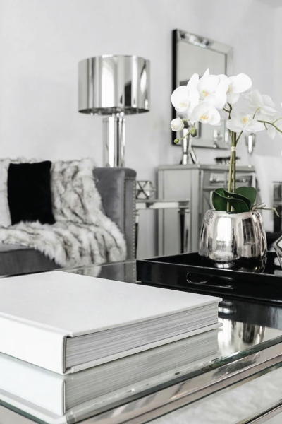 White book on a mirrored coffee table with white orchids and silver decor in a bright spring-inspired living room.