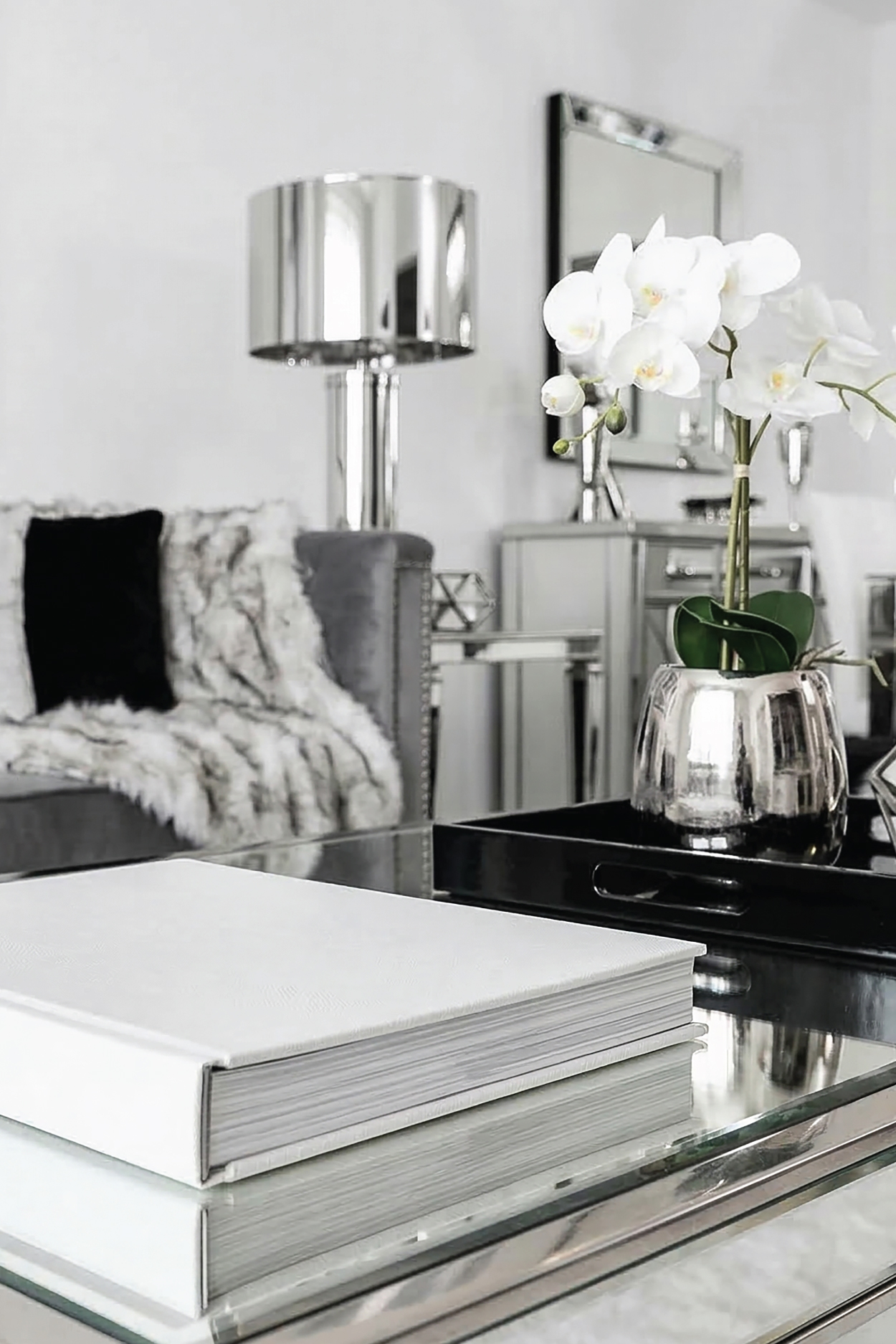 White book on a mirrored coffee table with white orchids and silver decor in a bright spring-inspired living room.