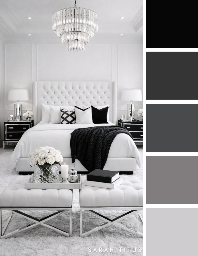 Luxe white bedroom with a tufted headboard, crystal chandelier, black throw blanket, silver lamps, and white roses in a black, white, gray, and silver color palette.