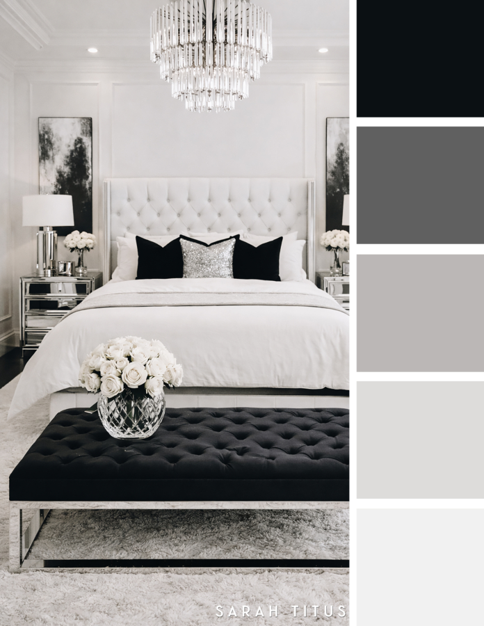 Elegant white bedroom with a white tufted bed, crystal chandelier, mirrored nightstands, black bench, white roses, and black accent pillows in a black, white, gray, and silver color palette.