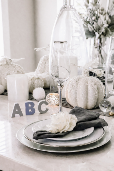 Glam black, white, and silver table setting with gray ABC letters, white pumpkins, and a white flower napkin ring.