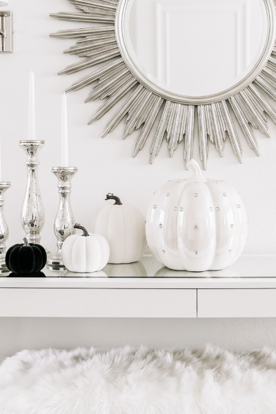 White halloween decor with pumpkins, candles and decorative mirror on shelf